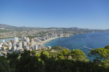 Akdeniz manzaralı dağ manzarası, mavi gökyüzü, yeşil ağaçlar ve güneşli yaz gününde İspanya 'nın Calpe plajı..