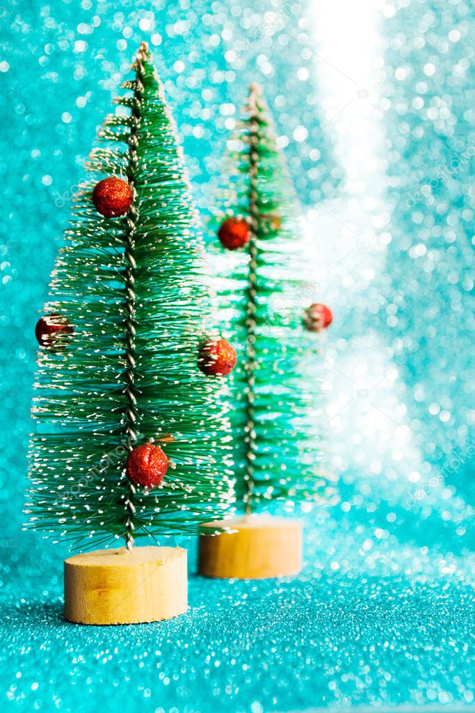 Two small Christmas decorative fir trees on a blue shiny glitter background. Festive christmas background.