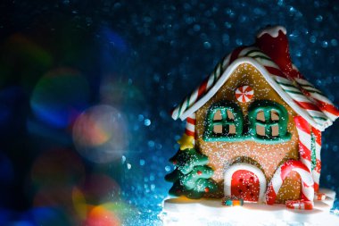 Noel oyuncağı, alttan aydınlatılmış zencefilli kek evi şeklinde holografik bir ışıltıyla mavi, parlak bir arka planda. Seçici odak.