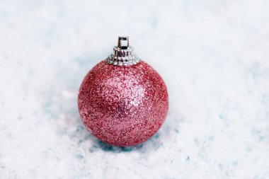 Beyaz karlı arka planda pembe parlak bir Noel oyuncağı. Seçici odak.