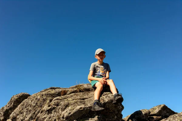 大きな岩の端に座っている少年山の夏のハイキング山の頂上. — ストック写真