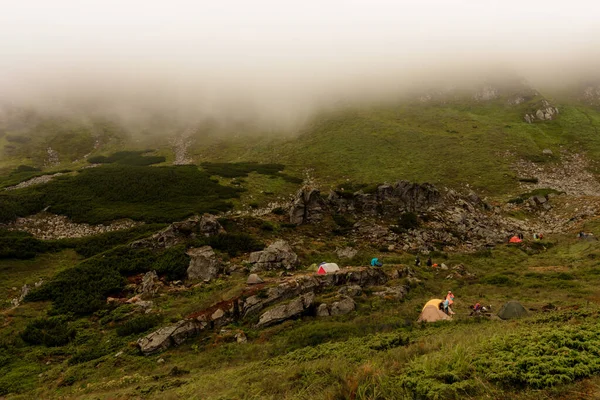A small tent town in the mountains, tents by the lake in the mountains, the area near the lake Brebeneskul, the Carpathian mountains, fog and rain in the mountains.2020