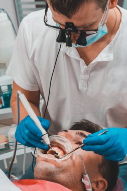 Klinikteki dişçi, tartar çıkarma prosedürü, dürbündeki dişçi hastanın ağzındaki tartartarı çıkarıyor. 2020