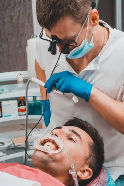 Diş hekimi, dişçi, hastanın ağzındaki tartar, tükürük püskürtücü ve retraktörü çıkarmak için gerekli aletleri hazırlar. 2020