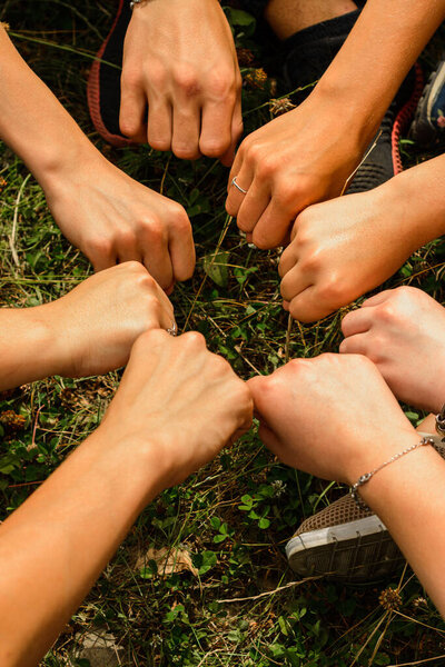 A group of young people made a circle with their fists on a background of grass, a symbol of unity, success and friendship.2020