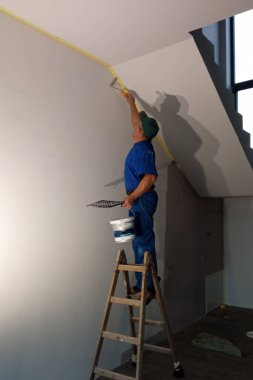 Duvarı beyaza boyayan bir adam, bir merdivenin üzerinde duruyor. 2020