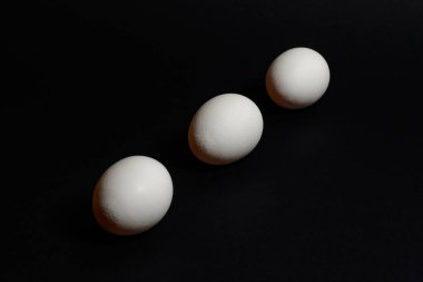 Siyah zemin üzerinde üç beyaz yumurta, 2021 proteini bakımından zengin beslenme ve sağlıklı yiyecekler.