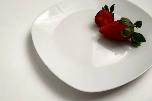 两个草莓在一个盘子里 一个草莓被咬 浆果在一个白光滑的盘子里 是登记的地方 — 图库照片