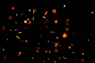 Siyah arka planda parlak sarı kıvılcımlar, sarı parlak yuvarlak bokeh. Yanan közlerin parçacıkları gece gökyüzünde tek başına uçar ve parlar..