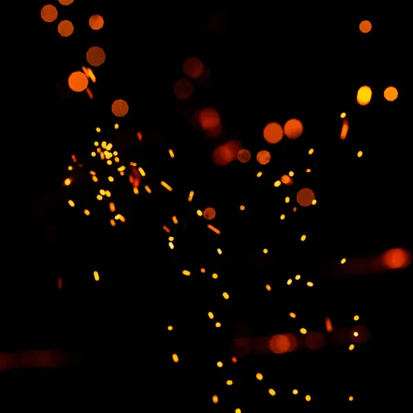 Bright yellow sparks on a black background, yellow bright round bokeh. Particles of burning embers fly and glow isolated in the night sky.