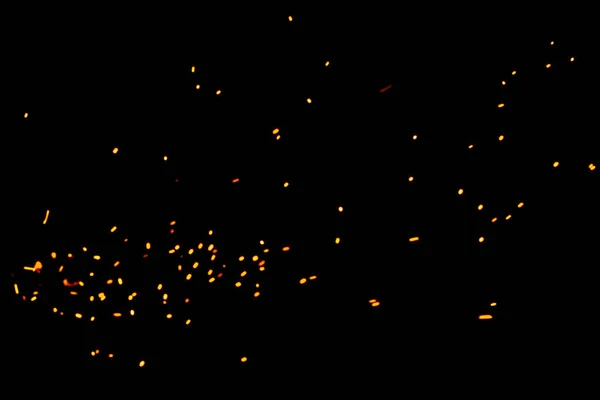 Natural yellow-hot sparks of fire on a black background, bright yellow bokeh from the fire. Particles of burning embers fly and glow isolated in the night sky.