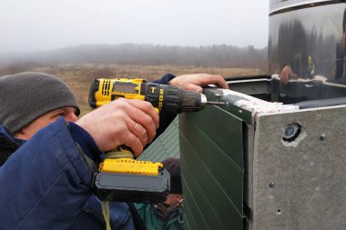 Yeni iki katlı bir evde yeni bir bacaya bakan işçiler, 2020 kışlık tulum giyip, bir sondaj bataryası kullanıyorlar..