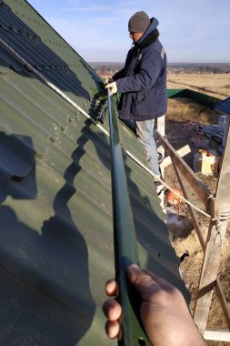 Usta, sigorta elementleri, yeşil çatı ve metal fayansların olmadığı bir çatıda çalışıyor. Kırsal kesimde özel bir ev..