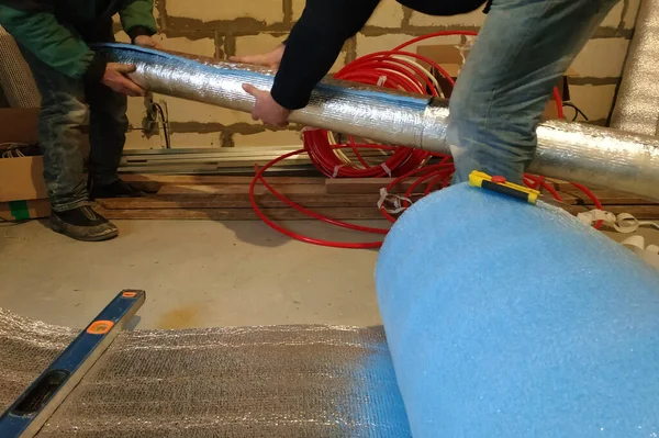 İşçiler yeni inşa edilen evde galvanizli boruları folyoyla sarıyorlar. Folyonun uzunluğunu ve genişliğini ölçün, sarın ve bantlayın. 2020