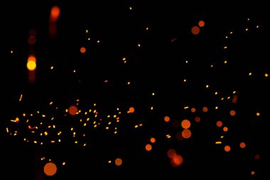 Siyah arka planda parlak sarı kıvılcımlar, sarı parlak yuvarlak bokeh. Yanan közlerin parçacıkları gece gökyüzünde tek başına uçar ve parlar..