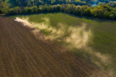Ukrayna toprakları bir traktör tarafından işleniyor, tarla tahıl ekilmeden önce ekiliyor, üst görünüm, ufukta bir orman görülebiliyor. 2021