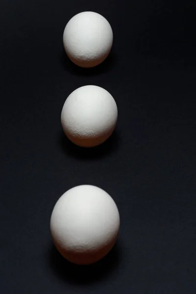 Eggs on a black background, three eggs in a row, shadow on the background of eggs, healthy and diet food.2020
