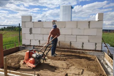 Titreşimli levha kullanılıyor, titreşimli levha yardımıyla kumu sıkıştırıyor, yeni bir ev inşa ediyor.