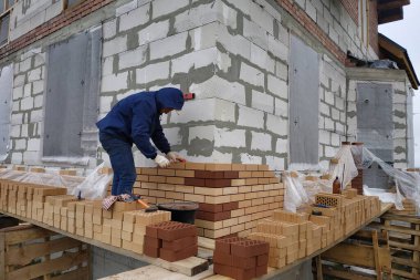 İşçi, evin duvarlarını kırmızı tuğlalarla örüyor. Yeni bir ev inşa etme süreci.