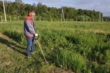 Adam çimleri biçme makinesiyle biçiyor, çayırda uzun otlar, bahçede el yapımı. Yeni