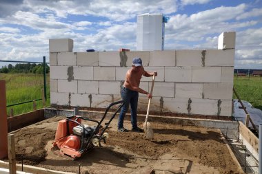 Titreşimli levha kullanılıyor, titreşimli levha yardımıyla kumu sıkıştırıyor, yeni bir ev inşa ediyor.