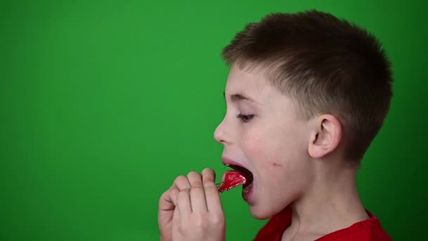 Barnet sätter en tallrik på tänderna, slow motion, sidovy av ett barn, en pojke på en grön bakgrund. — Stockvideo