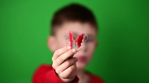 Placa para alinear los dientes, un niño sobre un fondo verde sosteniendo una placa, una placa dental en sus manos. — Vídeos de Stock