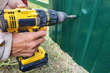 Tornavidayla çalışan işçi vidaları çitlere vidalıyor ve metal bir çit takıyor.