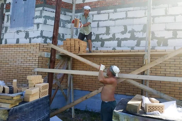 노동자가 노동자에게 벽돌을 던지고 개인적 지역에서 작업을 의나무 비계를 — 스톡 사진