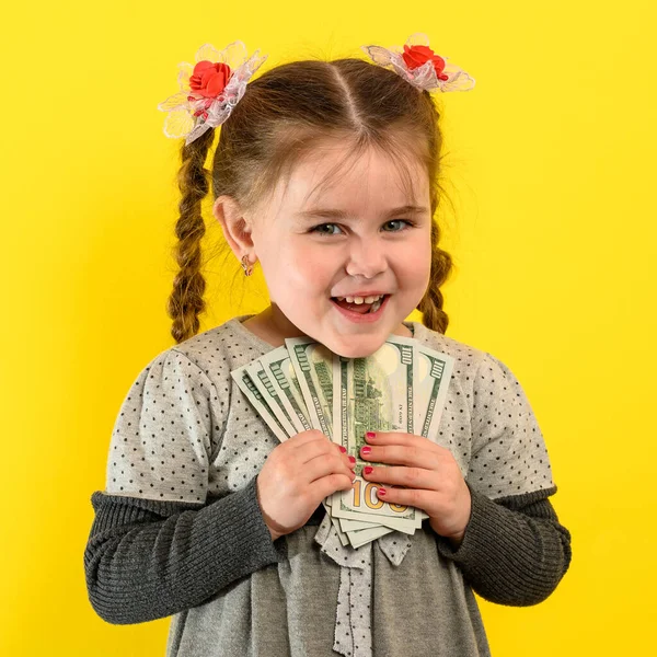 子供と経済的責任 黄色の背景の少女 彼女の手にドル 子供の金融リテラシー 新しい — ストック写真