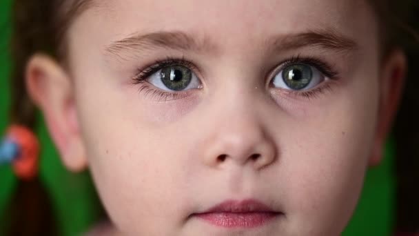 Little girl blinking eyes, slow motion of a child, portrait on a green background. — Stock Video