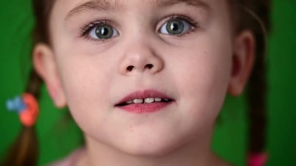 Κοριτσάκι που ανοιγοκλείνει τα μάτια, αργή κίνηση παιδιού, πορτραίτο σε πράσινο φόντο. — Αρχείο Βίντεο
