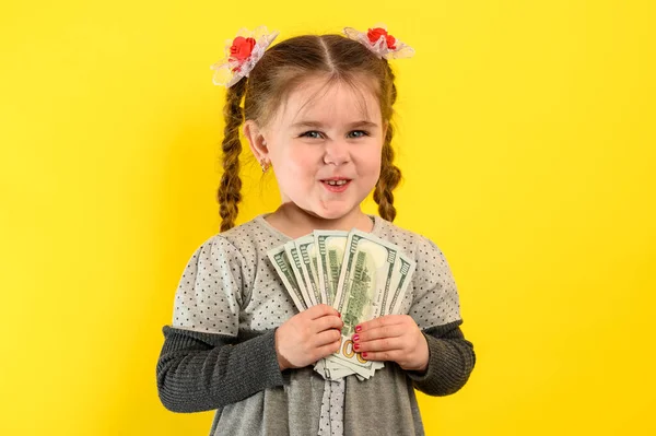 子供と経済的責任 黄色の背景の少女 彼女の手にドル 子供の金融リテラシー 新しい — ストック写真