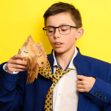 Acınası bakışlı bir çocuk elinde euro banknotları, sarı arka planda yetişkin takım elbiseli bir çocuk, mavi ceketli ve sarı kravatlı. yeni