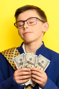 Gözlüklü ve kocaman takım elbiseli bir çocuk Amerikan doları, bir çocuk ve çok para tutuyor. yeni