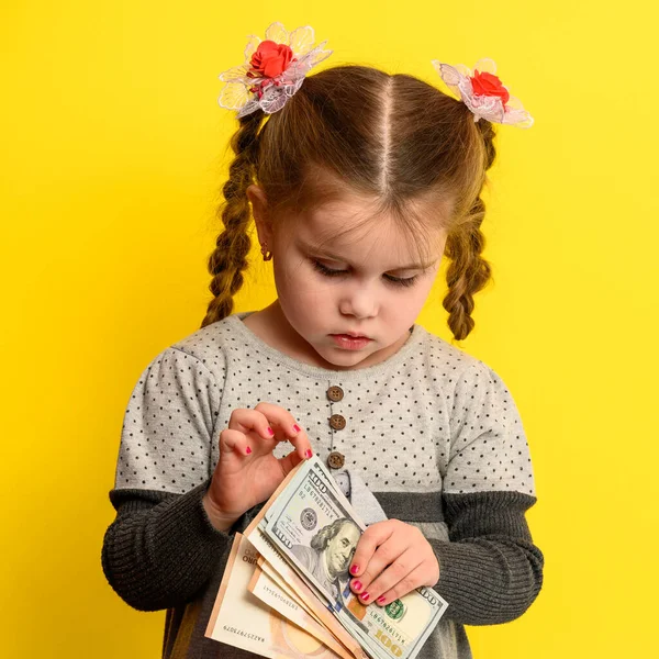 子供の金融セキュリティ 少女は手にお金 黄色の背景に子供の肖像画を保持します 新しい — ストック写真