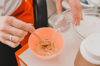 Güzellik uzmanı yüzüne sürmeden önce altın maskeyi karıştırır, maskeyi bir kasede karıştırır. yeni