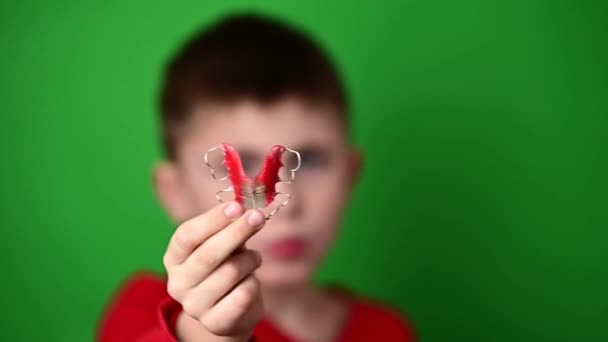 Lempeng untuk menyelaraskan gigi, seorang anak laki-laki dengan latar belakang hijau memegang piring, piring gigi di tangannya. — Stok Video