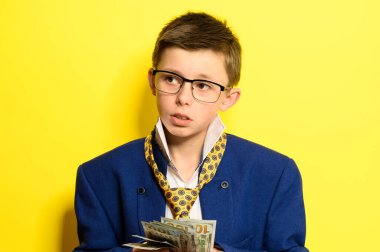 Sarı arka planda yetişkin kıyafeti giymiş bir çocuk, bir çocuğun elinde uluslararası para birikimi, gelecek için çocuk birikimleri. yeni