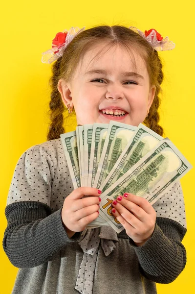 黄色の背景に少女の肖像画 彼の手の中にお金を保持子供 米ドルと子供の大規模な量 新しい — ストック写真