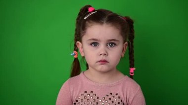 Yeşil arka planda bir kızın portresi, ağır çekimde üzgün bir çocuk bakışı..