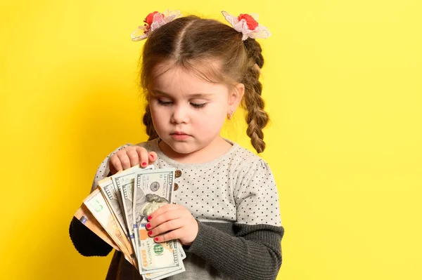 黄色の背景にかわいい女の子は子供の世界の通貨 金融リテラシーと開発を保持しています 新しい — ストック写真