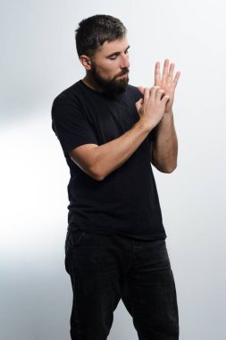 Koyu renk gömlek ve pantolon giyen sakallı bir adam elini ve parmaklarını açık gri zemine doğru dikkatlice inceliyor..