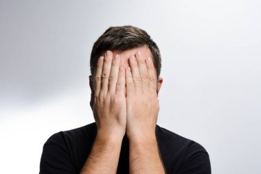 Bir adam ellerini arka planda tutarak yüzünü kapatır. Utanç, stres, umutsuzluk ya da hayal kırıklığını ifade eder..