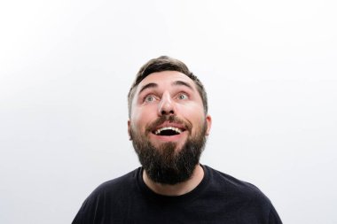 Sakallı bir adam beyaz bir arkaplan karşısında şaşırmış ve şaşırmış bir ifadeyle yukarı bakar. Onun açık ağzı ve geniş gözleri şaşkınlık iletir..