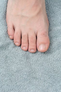 Yumuşak, gri bir havluda dinlenen bir insanın ayağının detaylı görüntüsü. Görüntü ayak parmaklarına ve havlunun dokusuna odaklanıyor..