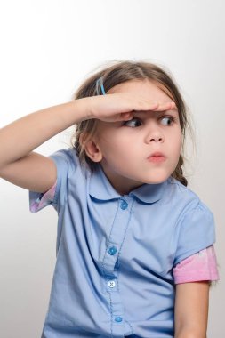 Meraklı bir çocuk uzak mesafeye bakıyor, eli gözlerini güneşten koruyor. Açık mavi bir gömlek giyiyor, düşünceli bir ifade sergiliyor..