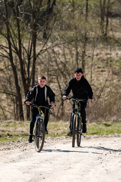 Dağ bisikleti süren iki genç çocuk ağaçlık bir alanda kirli bir patikadan aşağı iniyor. Güneş ışıl ışıl parlıyor, neşeli ve aktif bir sahne oluşturuyor..