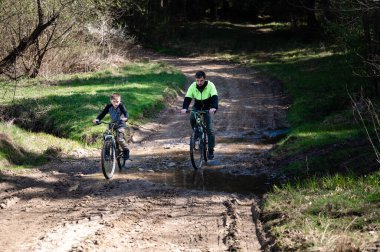 Bir adam ve küçük bir çocuk çamurlu bir yolda yol alarak su birikintilerini ve dengesiz araziyi dolaşırlar. Güneş ışığı ağaçların arasından süzülüp sıcak bir atmosfer yaratır..