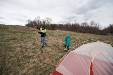 Bir baba ve çocuk çimenli bir alanda çadır kurmak için birlikte çalışırlar. Soğuk bir günde doğanın tadını çıkarırlar ve üzerlerinde bulutlu gökyüzü olan özel bir anı paylaşırlar..